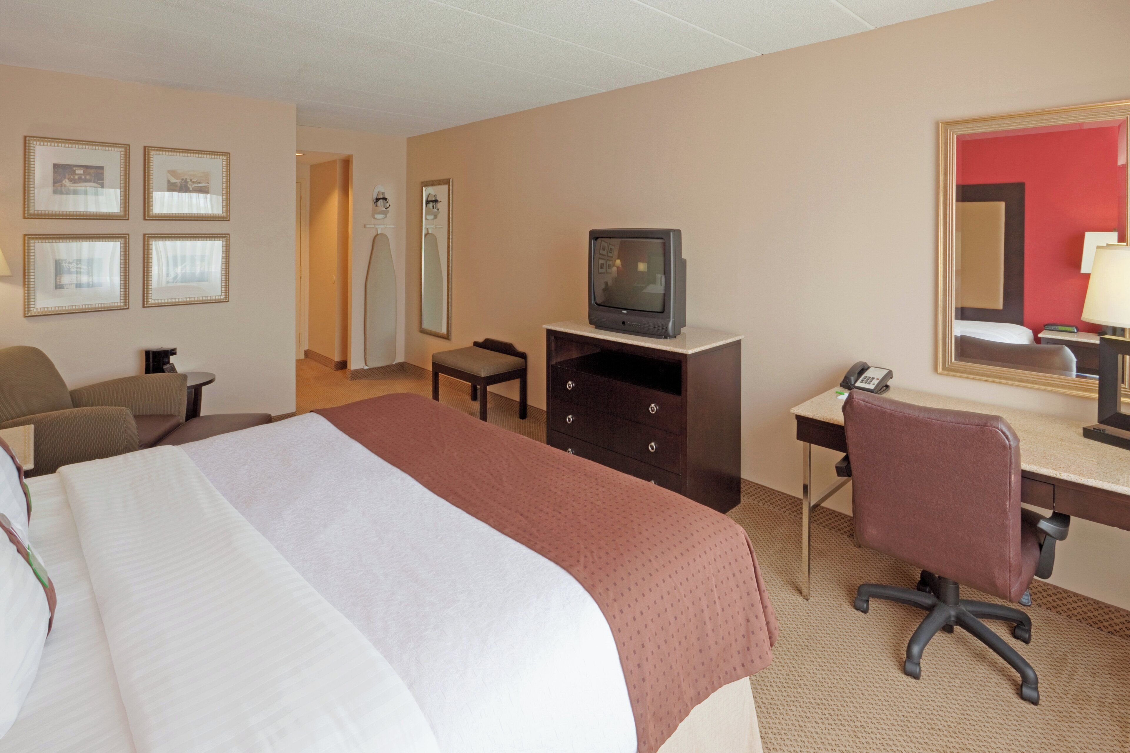 A hotel room with a bed, a desk, a chair, a television, and a mirror.