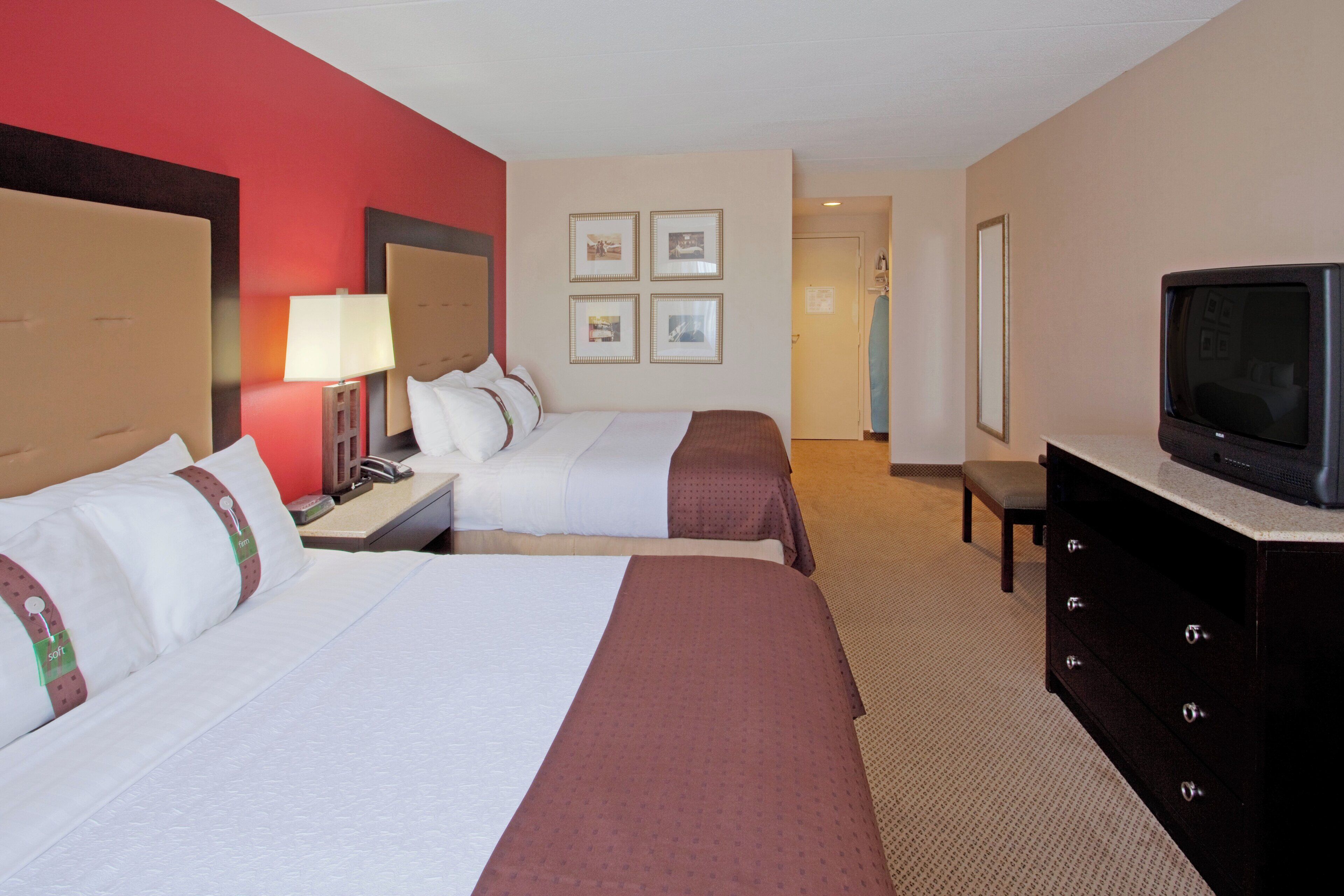A hotel room with two beds, a television, a desk, and a dresser.