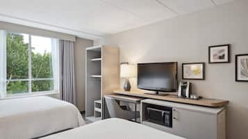 A hotel room with two beds, a desk with a television, a coffee maker, and framed pictures on the wall.