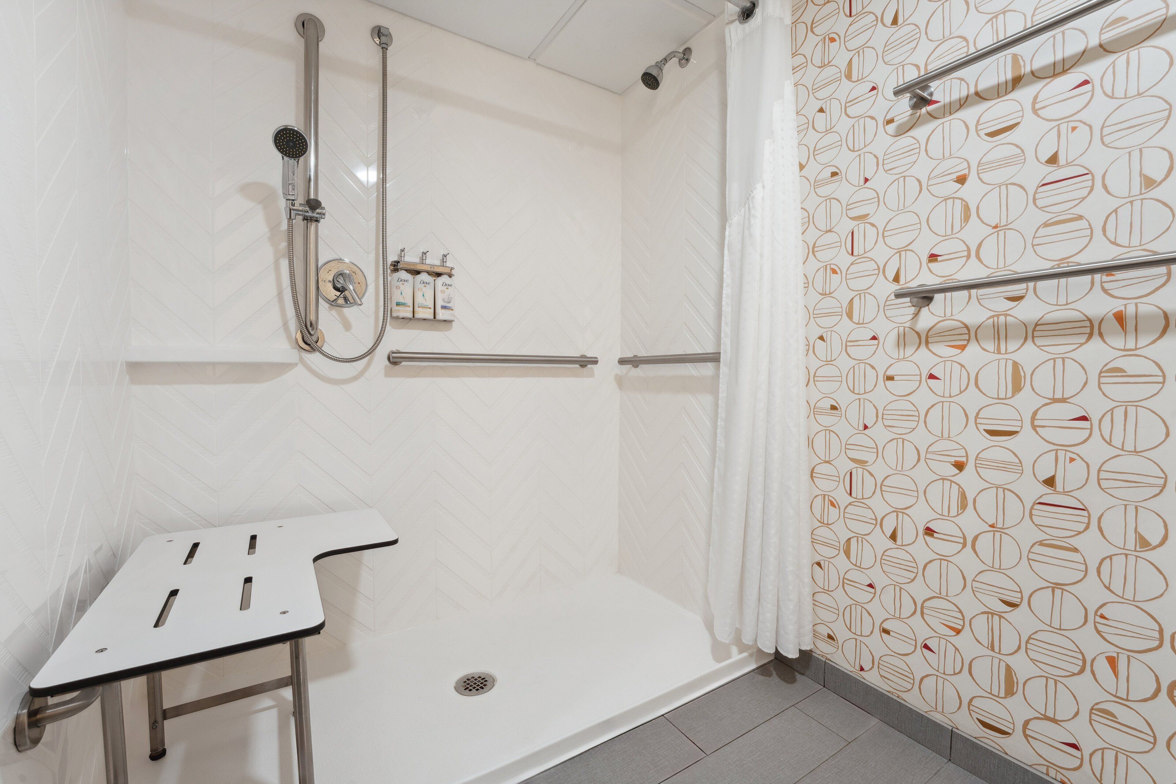 A shower area with a white tiled wall, a showerhead, a handheld shower, a towel rack, and a small table.