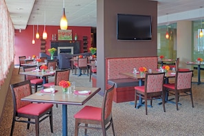 Un restaurante con cabinas y mesas, un televisor de pantalla plana en la pared y una alfombra estampada.
