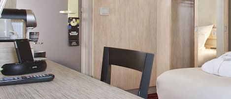 A hotel room with a bed, a desk with a phone and a coffee maker, a chair, a coat rack, and a wardrobe.