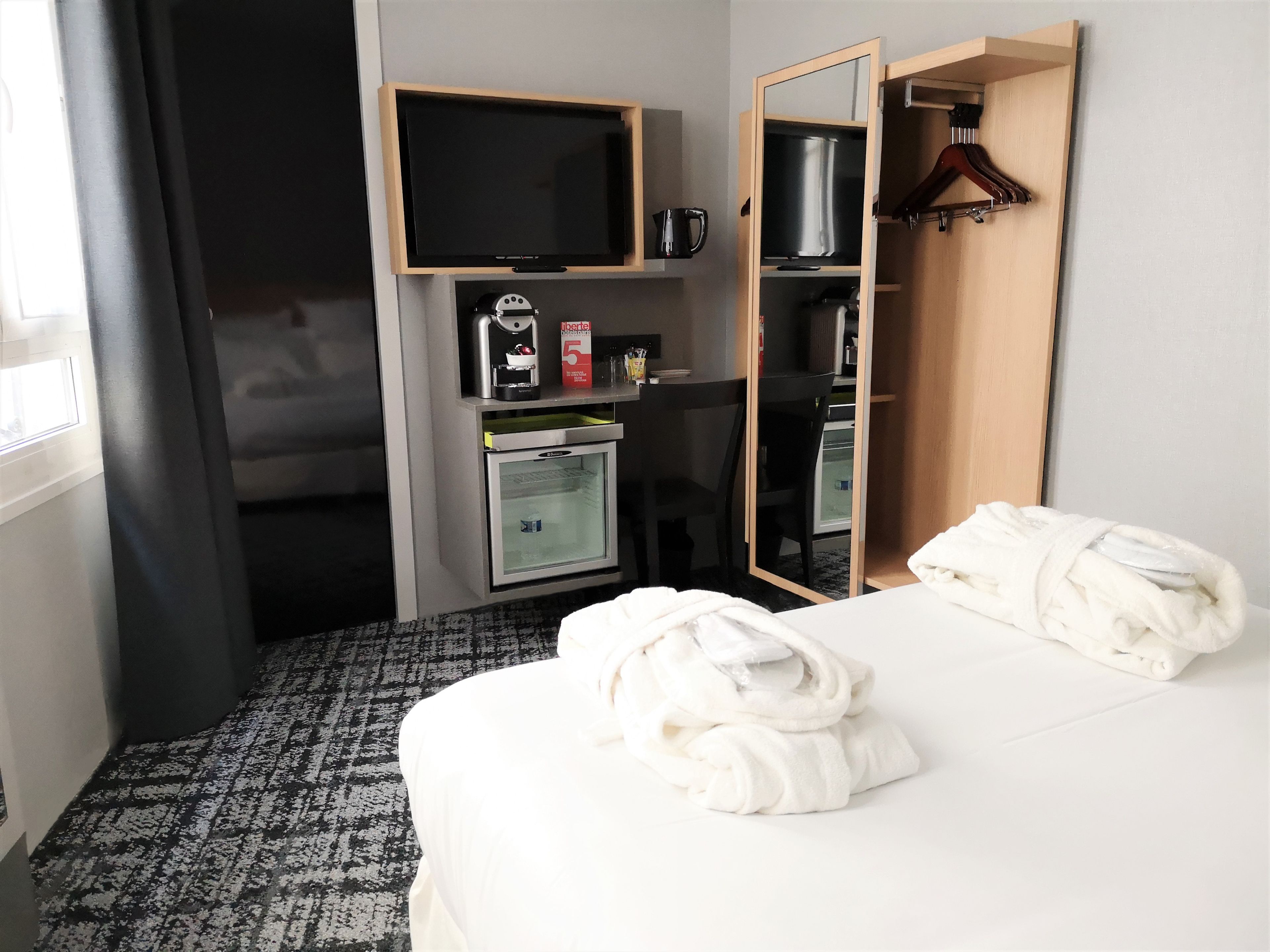 A hotel room with a bed, a TV, a minibar, a coffee machine, and a mirror.
