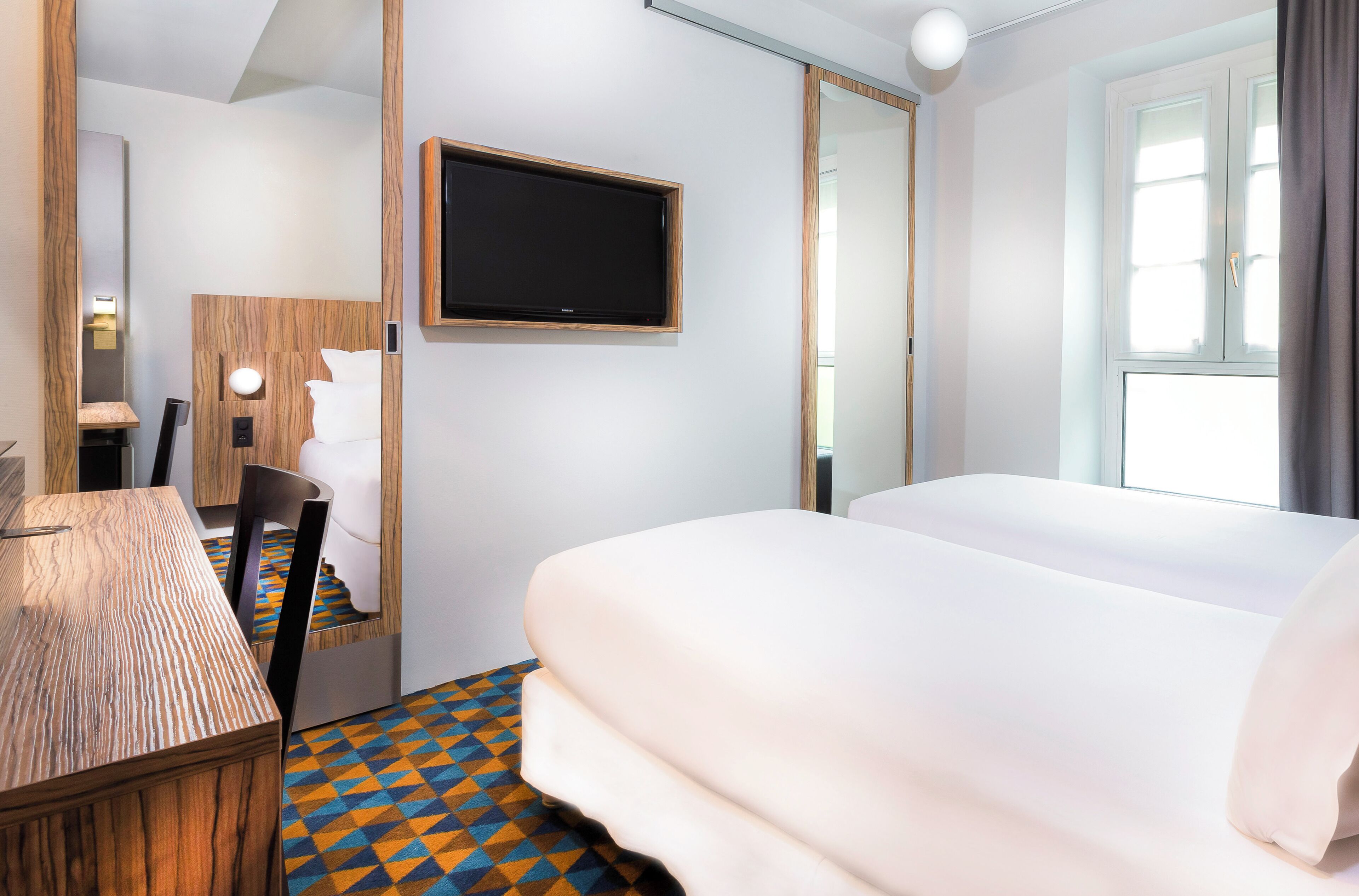 Una habitación de hotel con cama, escritorio, silla, televisor y ventana.