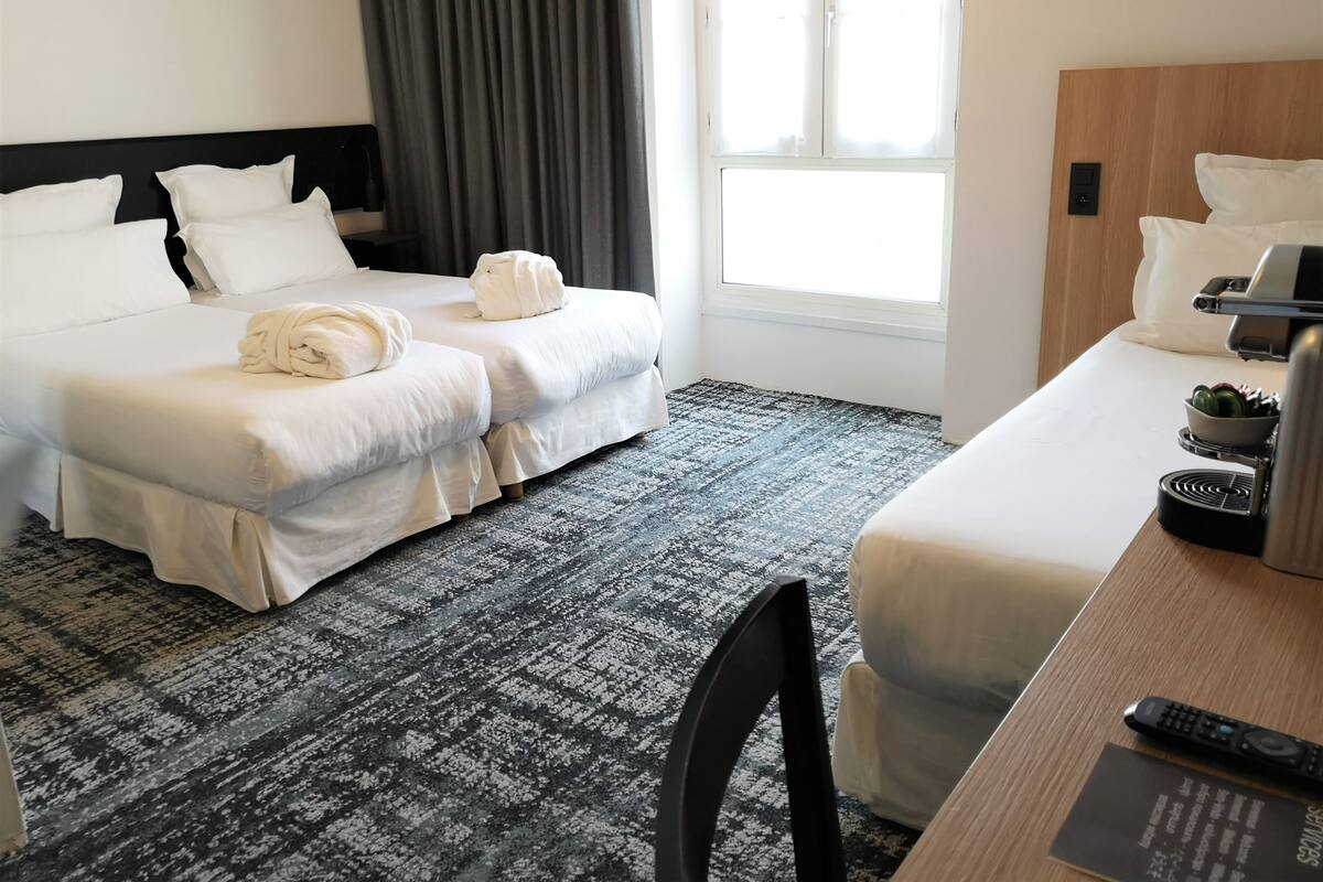 Hotelkamer met twee bedden, een bureau, een stoel, een koffieapparaat en een raam met gordijnen.
