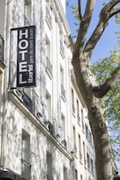 Un letrero de hotel con el nombre "HOTEL Libertel du Nord sudde" sobre una fachada blanca con balcones y un árbol en primer plano.