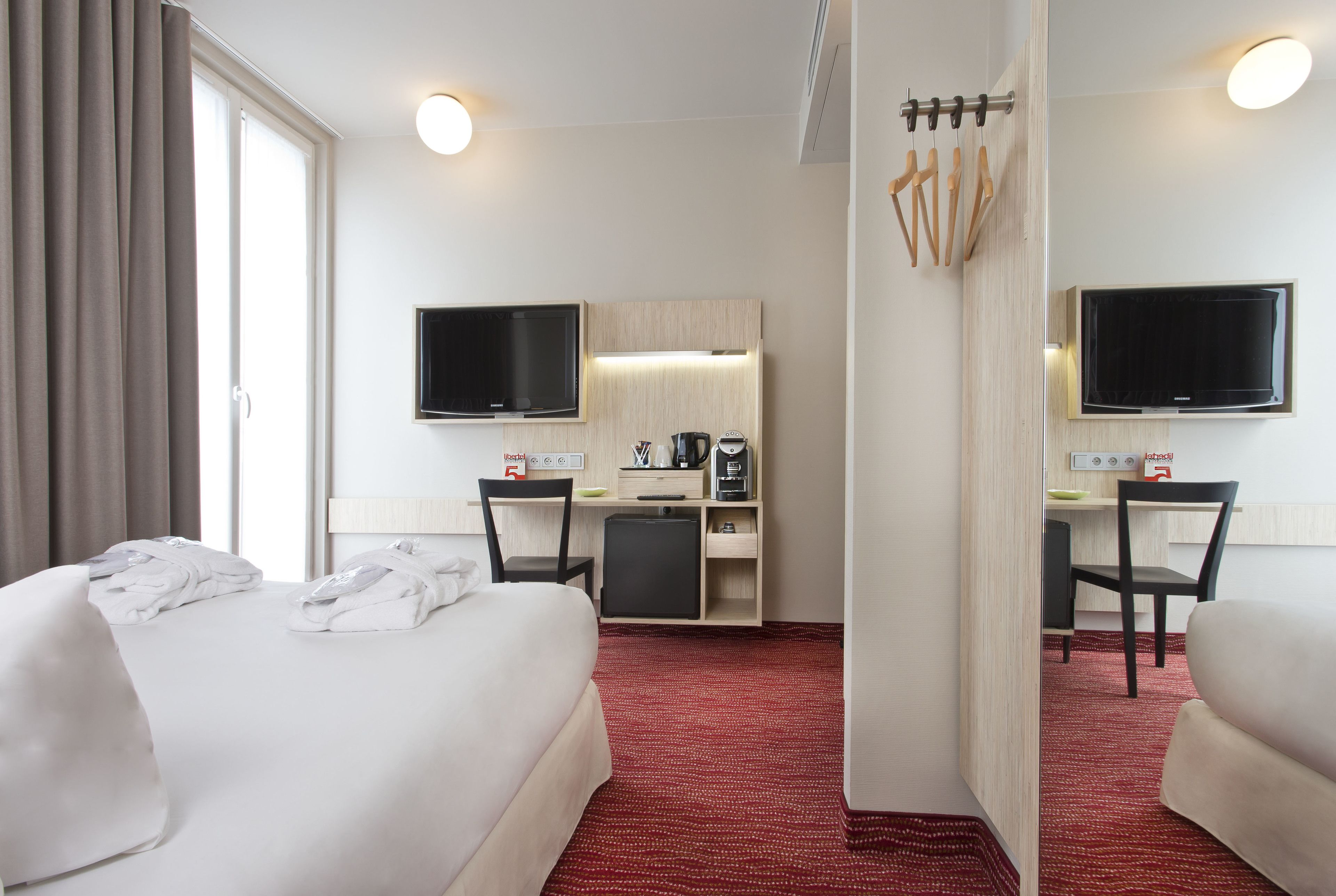 Una habitación de hotel con cama, escritorio, computadora, televisión y cafetera.