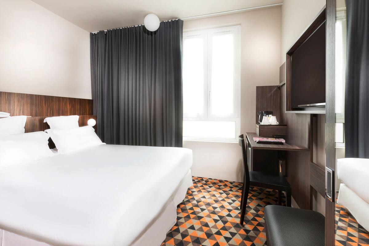 Een hotelkamer met een groot bed, een bureau met een televisie en een raam met gordijnen.