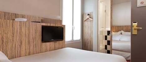 Habitación de hotel con dos camas, un televisor montado en la pared, una puerta corredera al baño y un panel de pared de madera.