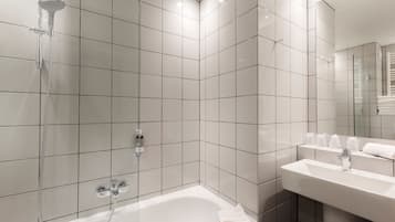A modern bathroom with white tiles, a glass-enclosed shower, a white sink, and a mirror.