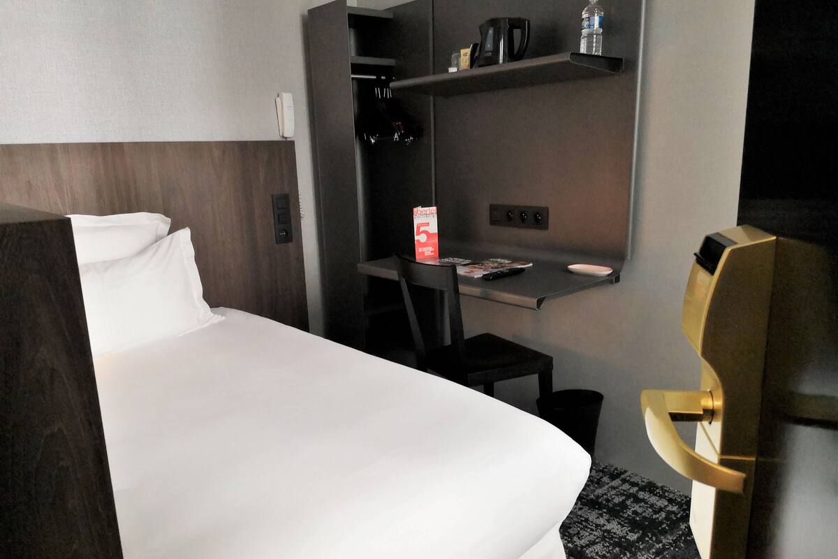Hotelkamer met een bed, bureau, stoel, minibar en deur met hendel.