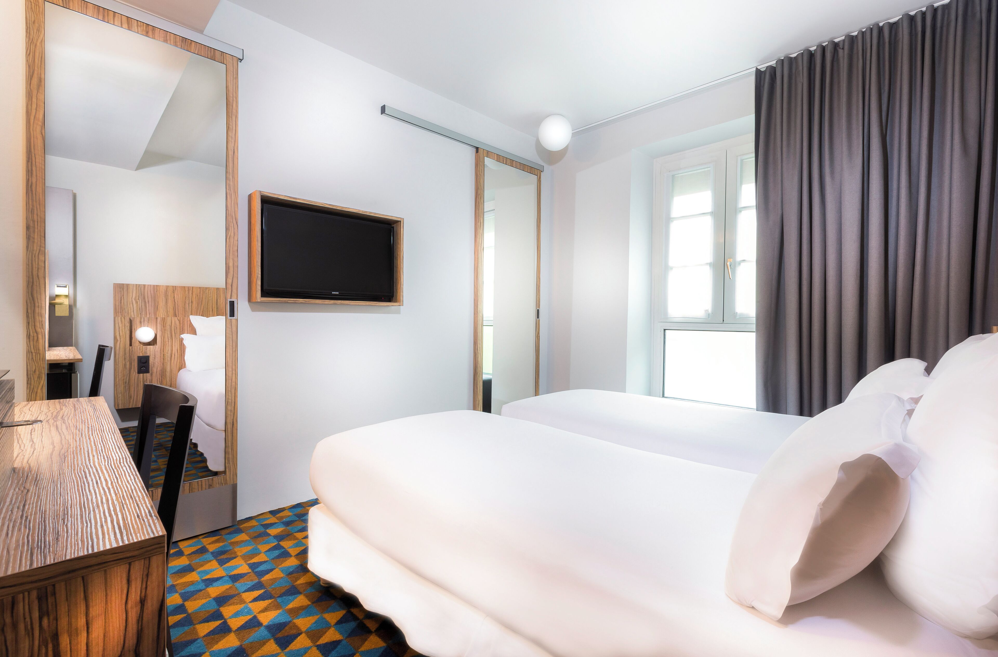 Habitación de hotel con cama, escritorio, silla, televisor y ventana con cortinas.