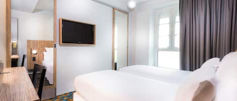 Habitación de hotel con cama, escritorio, silla, televisor y ventana con cortinas.