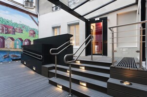 Una serie de escaleras exteriores con barandillas de metal que conducen a un espacio cubierto con vistas a un mural que representa casas y una masa de agua.