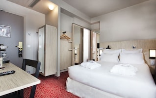 Una habitación de hotel con una cama, un escritorio, una silla, un armario y un espejo.