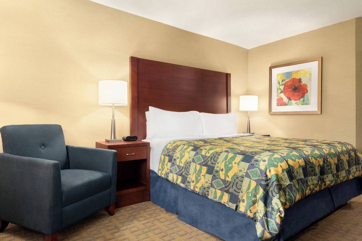 Una habitación de hotel con una cama, una silla, una mesita de noche y una lámpara.
