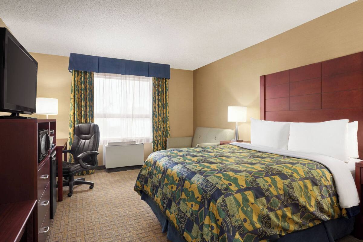 Una habitación de hotel con cama, escritorio con computadora, silla, televisor y ventana con cortinas.