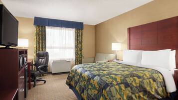 A hotel room with a bed, a desk with a computer, a chair, a television, and a window with curtains.