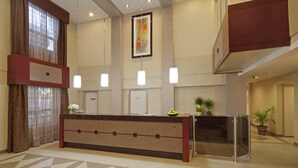 Zona de recepción de un hotel con mostrador, una obra de arte enmarcada encima y una escalera que sube a un nivel superior.
