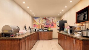 Una cocina moderna con armarios de madera, una estación de café de acero inoxidable, un microondas y un mural grande en la pared.