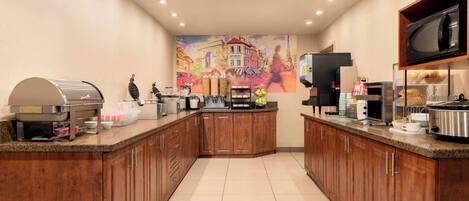 A modern kitchen with wooden cabinets, a stainless steel coffee station, a microwave, and a large mural on the wall.
