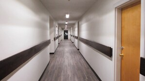 Um corredor comprido e estreito, com paredes brancas e detalhes escuros, que leva a uma porta no final.