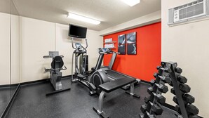 A gym with exercise equipment, a television, and a red accent wall. - Travelodge Suites by Wyndham Regina / Eastgate Bay (Regina)