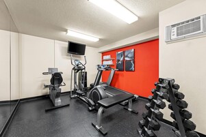 Un gimnasio con equipo de ejercicio, un televisor y una pared roja decorativa.
