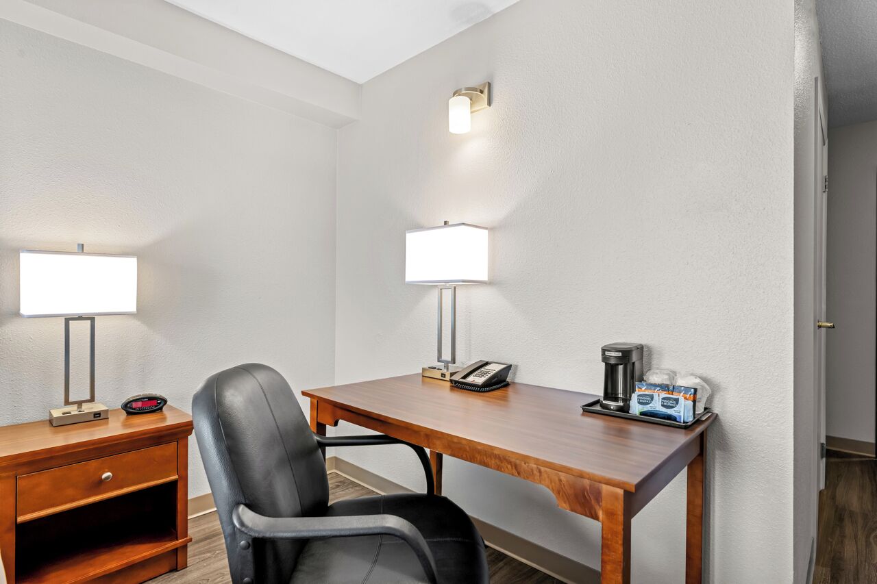 Ett hotellrum med ett skrivbord i trä, två lampor, en stol, en telefon, en kaffebryggare och en liten byrå med lådor.