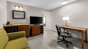 A hotel room with a kitchenette, a TV, a desk with a chair, and a lamp. - Travelodge Suites by Wyndham Regina / Eastgate Bay (Regina)