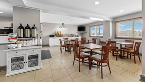 A modern dining area with a white counter, multiple chairs, and a television. - Travelodge Suites by Wyndham Regina / Eastgate Bay (Regina)