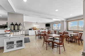 A modern dining area with a white counter, multiple chairs, and a television. - Travelodge Suites by Wyndham Regina / Eastgate Bay (Regina)