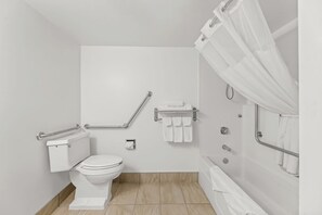 Une salle de bain moderne équipée de toilettes, de barres d’appui, d’une douche avec rideau et d’un porte-serviettes.