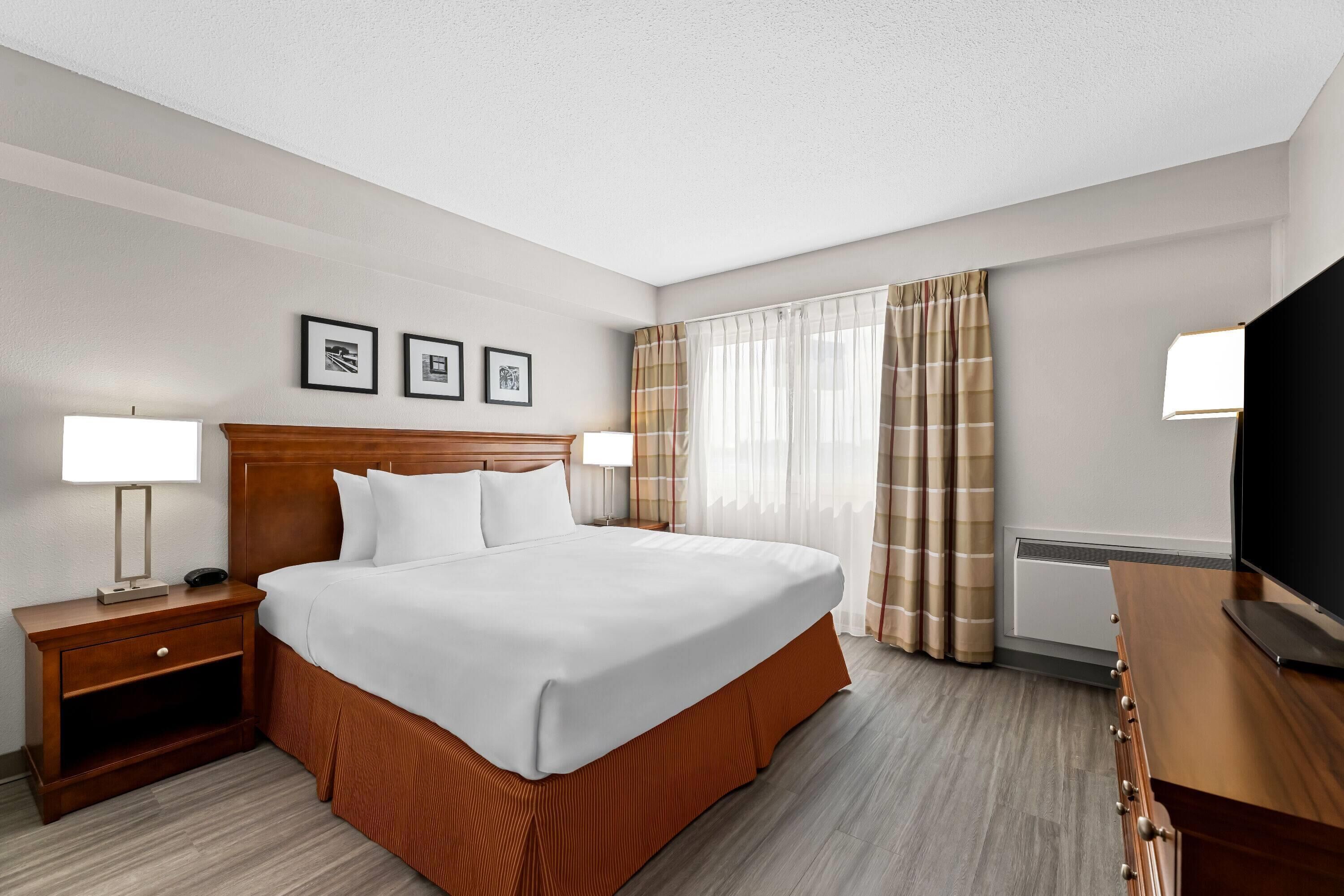 A hotel room with a large bed, two bedside tables, a TV, and a window with curtains.