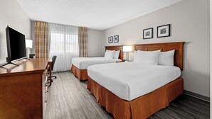 A hotel room with two beds, a desk, a TV, and a window with curtains. - Travelodge Suites by Wyndham Regina / Eastgate Bay (Regina)