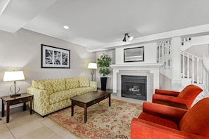 A living room with a sofa, armchair, coffee table, fireplace, and staircase. - Travelodge Suites by Wyndham Regina / Eastgate Bay (Regina)