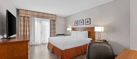 Een hotelkamer met een bed, een bureau, een stoel, een televisie, een lamp en een raam met gordijnen.