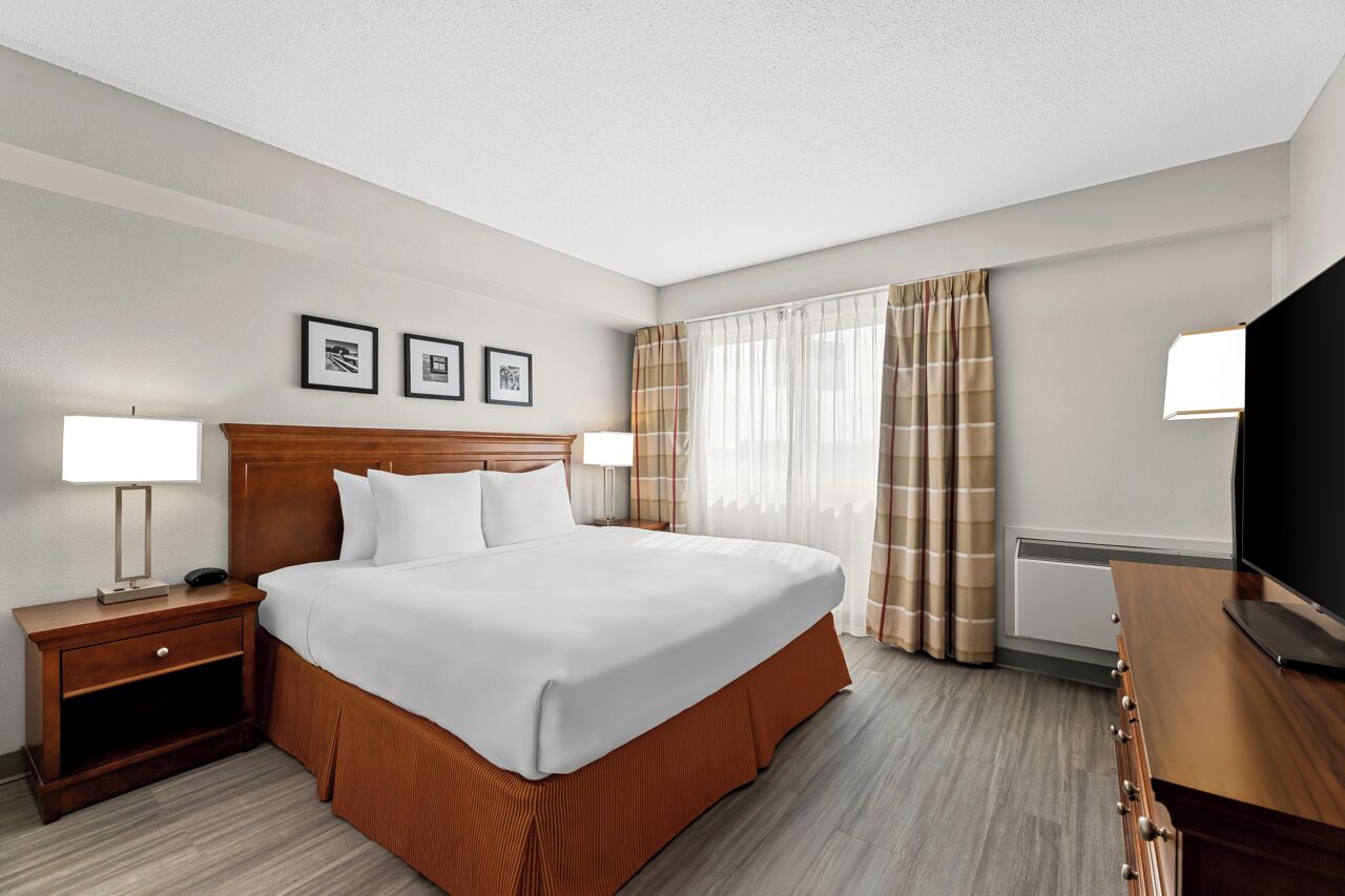 Une chambre d’hôtel avec un grand lit, deux tables de chevet avec des lampes, un téléviseur à écran plat et une fenêtre avec des rideaux.