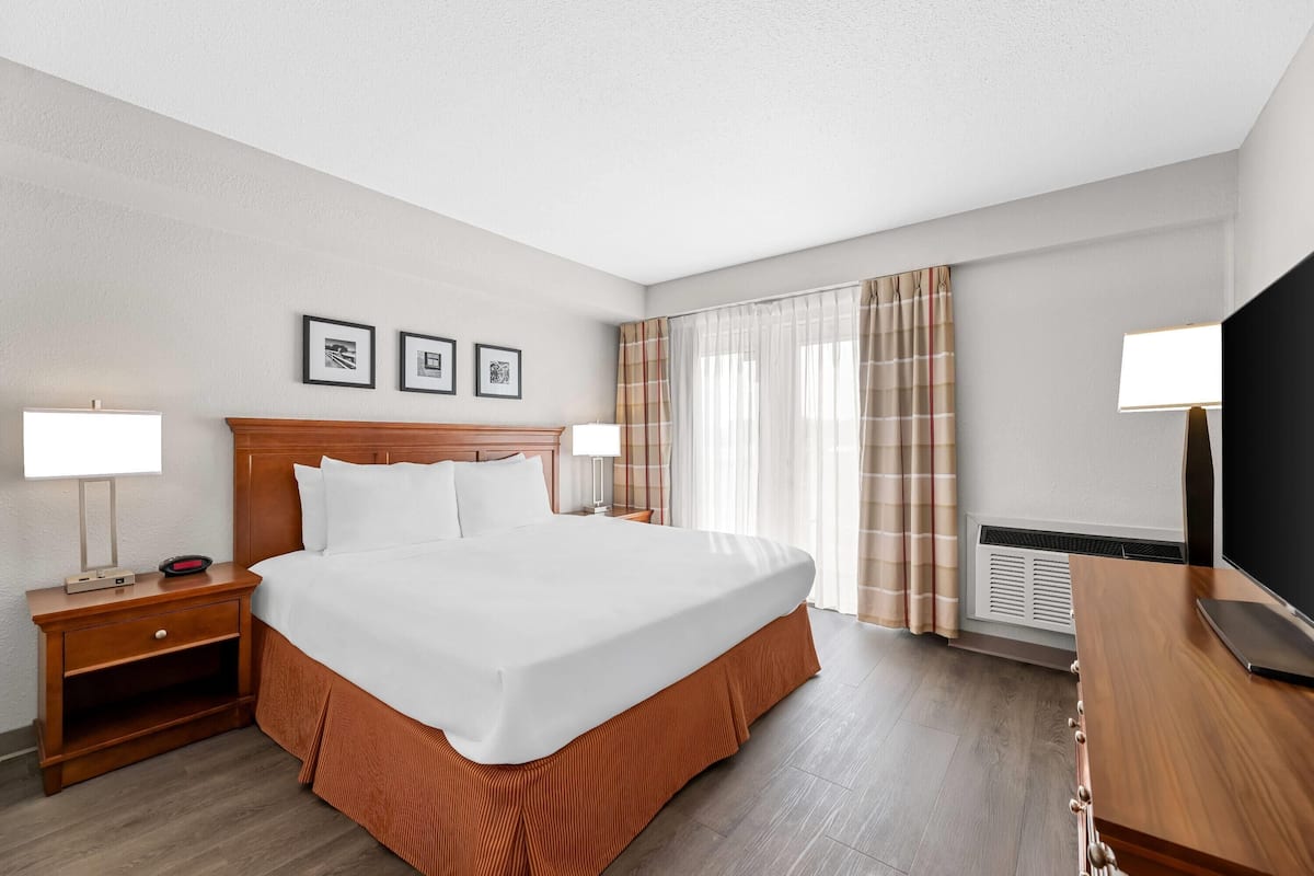A hotel room with a large bed, two bedside tables, a flat-screen TV, and a window with curtains.