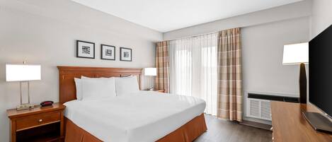 Una habitación de hotel con una cama grande, dos mesitas de noche, un televisor de pantalla plana y una ventana con cortinas.