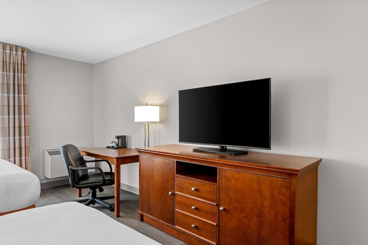 A hotel room with a bed, a desk with a television, a chair, and a lamp.