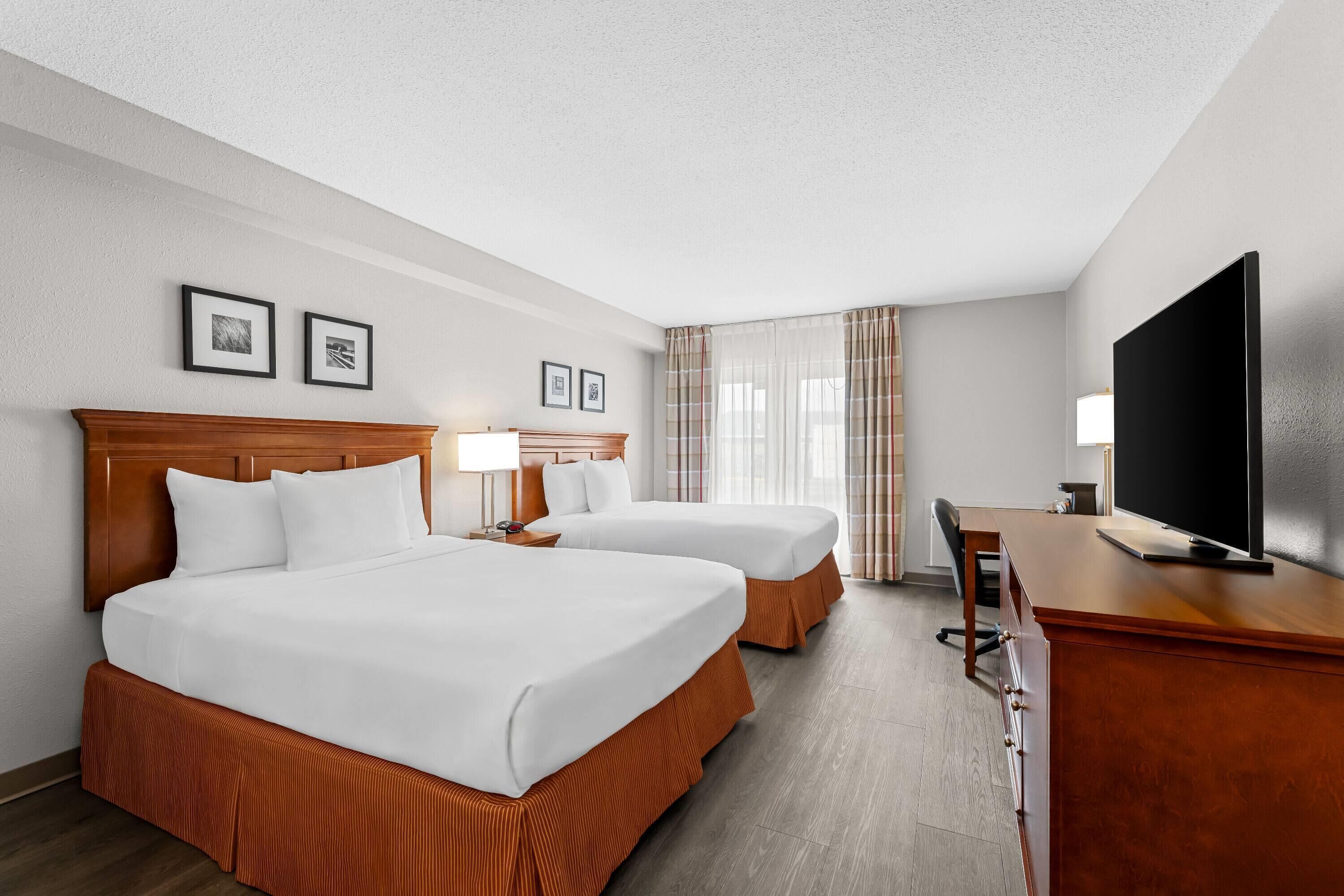 Een hotelkamer met twee bedden, een bureau, een televisie en foto’s in lijsten aan de muur.