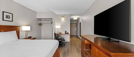 Una habitación de hotel con cama, escritorio, silla, televisor y armario.
