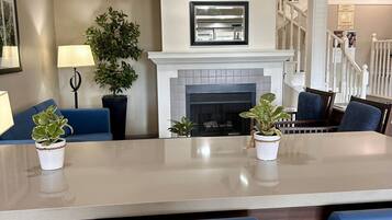 A modern living room with a fireplace, a dining table with chairs, and a staircase leading to another floor.