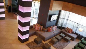 A modern lounge area with a sectional sofa, multiple seating options, and a large window providing natural light. - Hotel Huntington Beach (Huntington Beach)