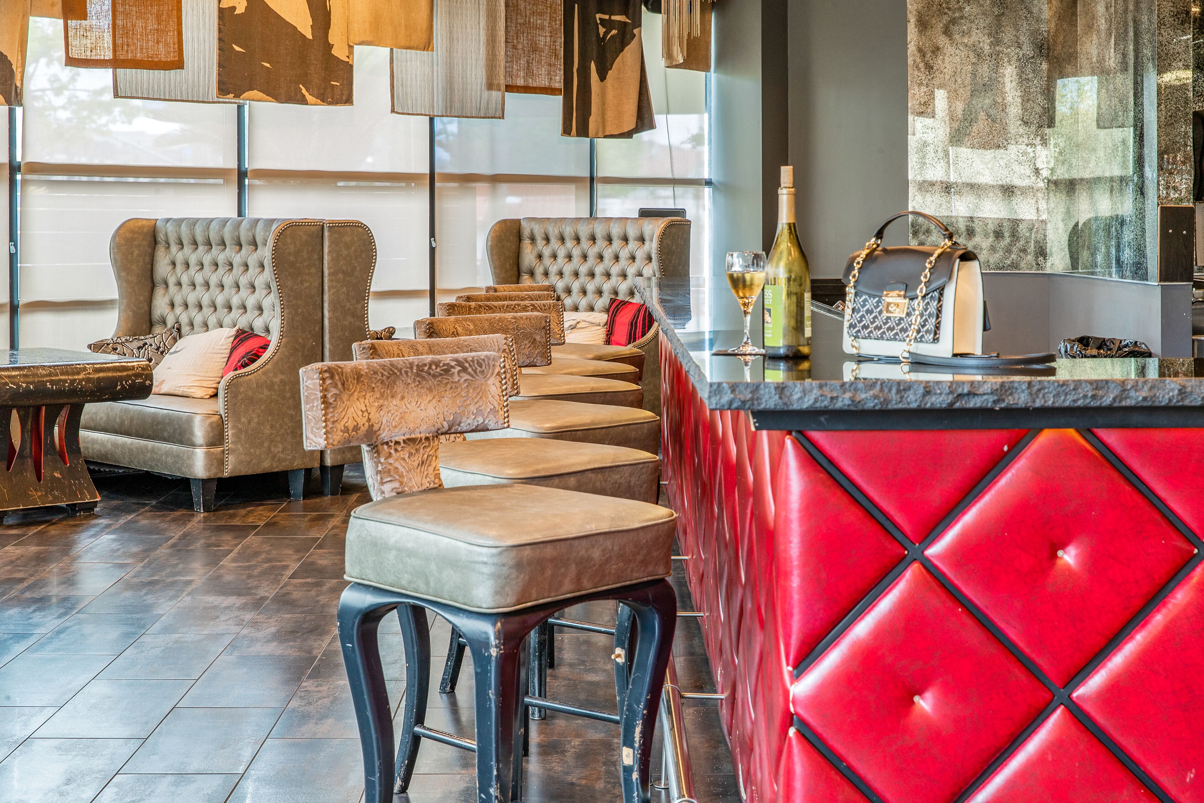 A bar area with leather sofas, a red cushioned bar counter, and a bottle of wine on the counter.