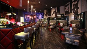 A bar area with red cushioned seating, a counter with a variety of bottles, and hanging abstract art. - Hotel Huntington Beach (Huntington Beach)