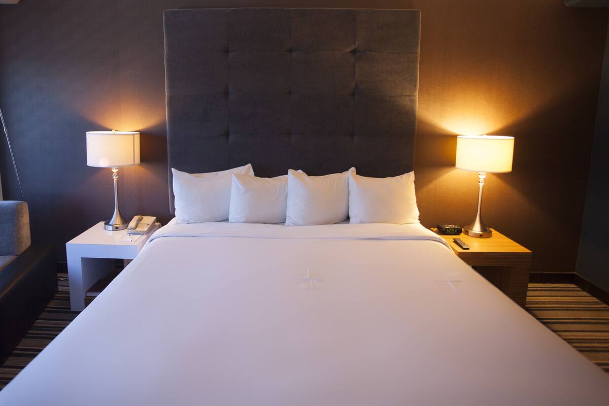 A hotel room with a large bed, two bedside tables with lamps, a telephone, and a chair.