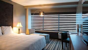 A hotel room with a large bed, a desk with a chair, a lamp, and a window with blinds.
