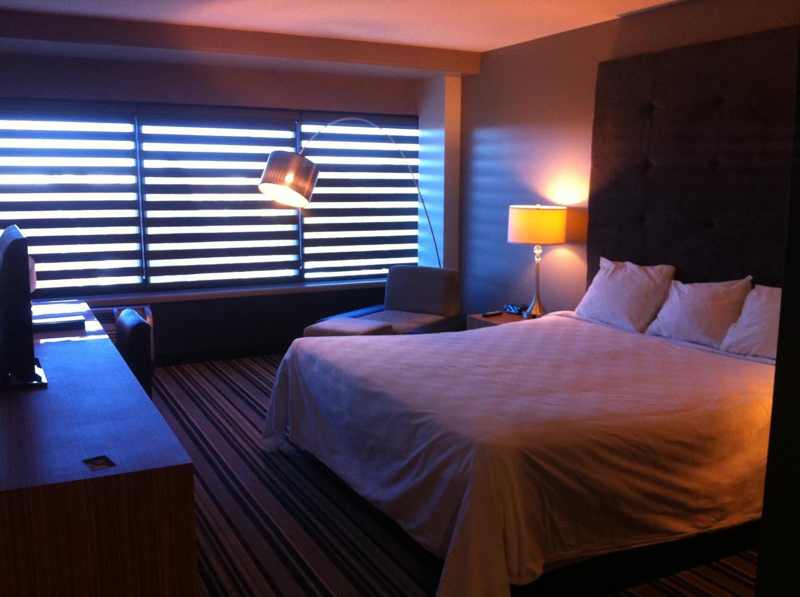 Una habitación de hotel con cama, escritorio, silla, lámpara y televisión.